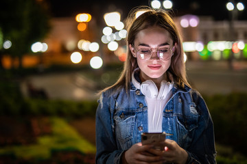 Outdoor portrait of beautiful young woman using her mobile phone at night.