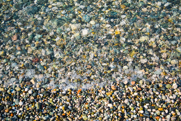Colorful sea stones lie in the waves of the surf