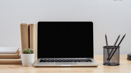 The dark screen of a modern laptop on the desktop with various objects, on a white wall background.Mockup.