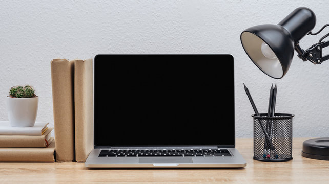 Dark laptop screen on the desktop with various objects, on a white wall background.Mockup.