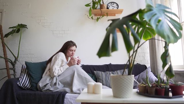 Scandinavian lifestyle - young beautiful woman resting on a couch, drinking coffee and enjoying life