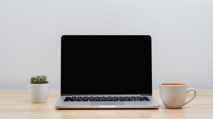 A workplace in the office with a dark laptop screen, a cup of coffee and a cactus.Mockup.