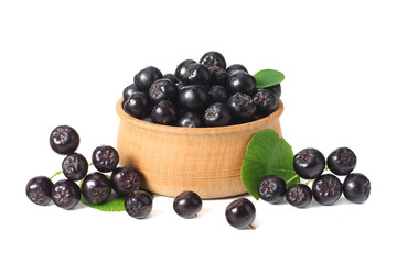 Chokeberry in wooden bowl with green leaves isolated on white background. Black aronia
