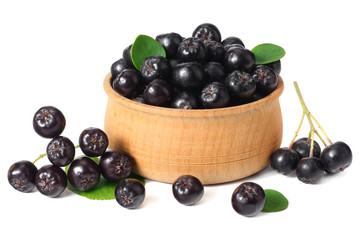 Chokeberry in wooden bowl with green leaves isolated on white background. Black aronia