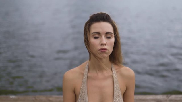 Fit slim woman practicing yoga exercises wearing mini swimsuit bikini at lake with clouds - Yoga meditation and wellness lifestyle concept - Close up to mid sitting shot