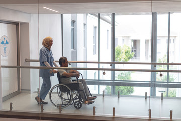 Female doctor pushing male patient in wheelchair at corridor - Powered by Adobe