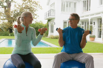 Active senior couple exercising with dumbbell in porch at home