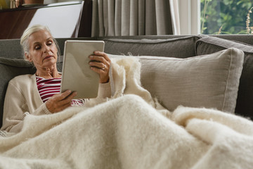 Active senior woman relaxing on sofa and using digital tablet in living room