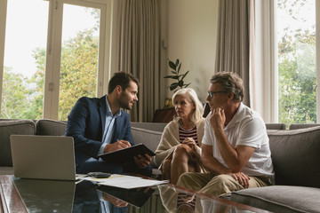 Active senior couple discussing with real estate agent over documents in living room