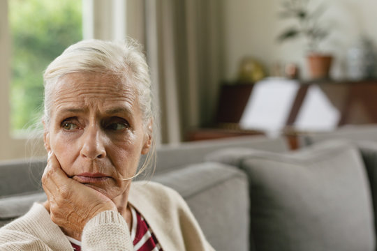 Active senior woman with hand on face sitting on sofa in a comfortable home