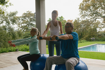 Female trainer assisting active senior couple to exercise with dumbbell in the porch