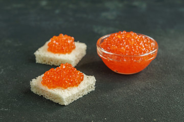 Square shaped wheat bread with red caviar on gray background