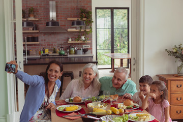 Multi-generation family taking selfie with mobile phone while having food on dining table