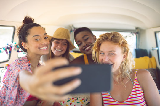 Group of female friends taking selfie with mobile phone in a camper van at beach