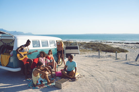 Group of friends having fun near camper van at beach