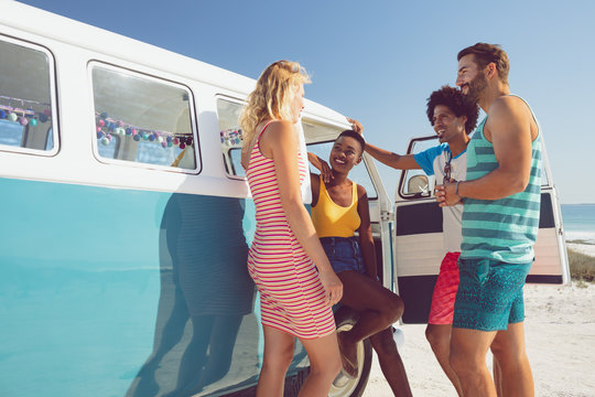 Group of friends talking with each other near camper van at beach in the sunshine