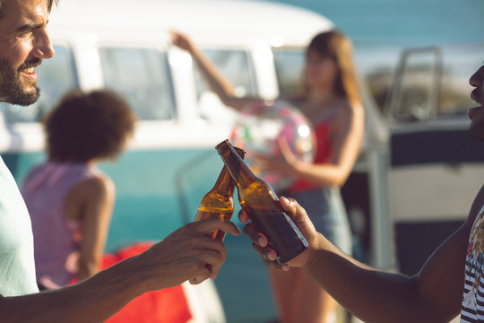 Male friends toasting beer bottle near camper van at beach