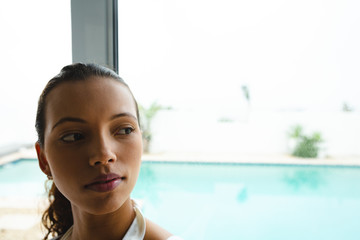 Thoughtful woman looking through window in living room at home