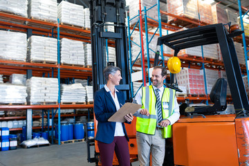 Male and female staff interacting with each other near forklift in warehouse
