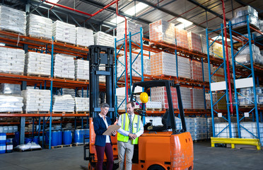 Male and female staff working together near forklift in warehouse