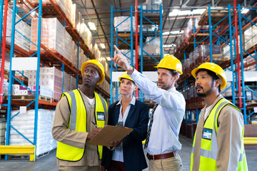 Male supervisor standing with coworkers and pointing at distance in warehouse - Powered by Adobe
