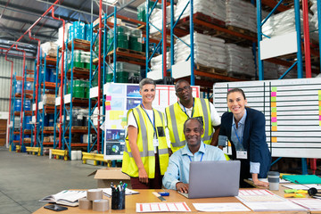 Male supervisor with his coworkers discussing over laptop at desk in warehouse
