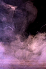Conceptual image of multi-colored smoke isolated on dark black background and wooden table.