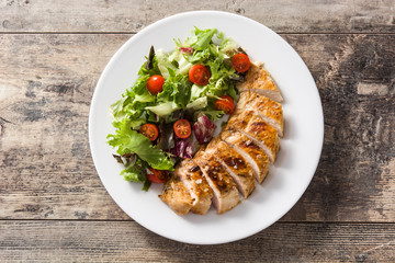 Grilled chicken breast with vegetables on a plate on wooden table. Top view.