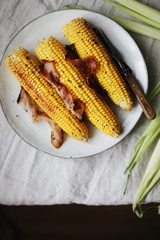 corn on the cob baked with butter, bacon and herbs on linen grey tablecloth