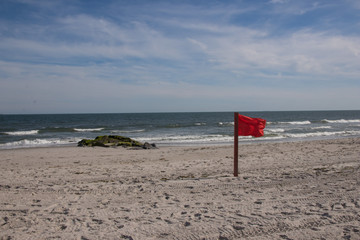 Warning sign of a red flag at a beautiful beach with a blue sky , Long Beach, New York, USA