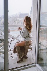 Woman drinking coffee or tea.Young girl with cup of coffee sitting on balcony with city view in morning.