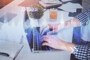 Double exposure of graph with man typing on computer in office on background. Concept of hard work.