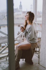 Woman drinking coffee or tea.Young girl with cup of coffee sitting on balcony with city view in morning.