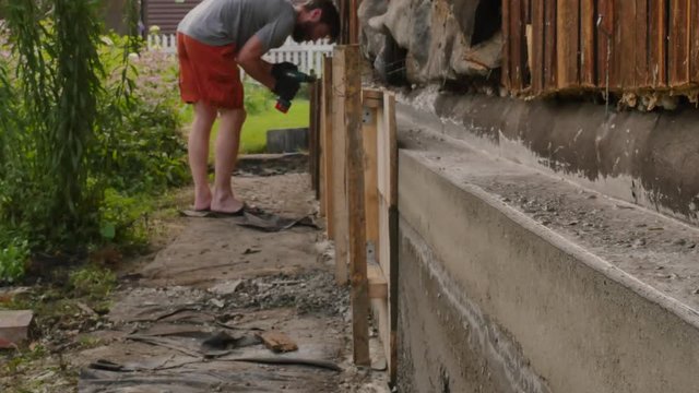 worker dismantles the wooden formwork, new foundation for old house. 4K