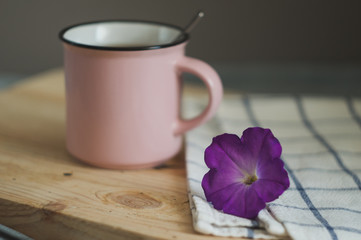 Pink cup of black tea with purple petunia flower on a wooden tray on a gray background
