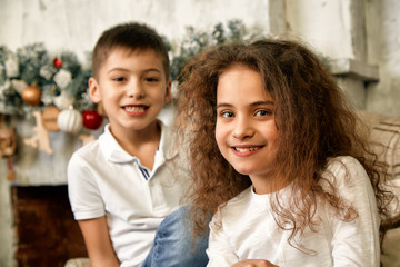 Portrait of children at Christmas waiting for gifts on a background of a fireplace decorated with New Year decor. Concept Christmas and children waiting for a miracle.