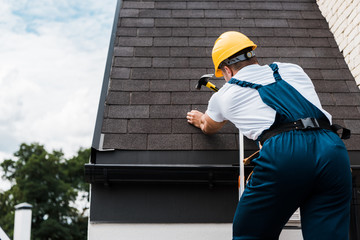 back view of handyman in uniform and helmet repairing roof while standing on ladder © LIGHTFIELD STUDIOS