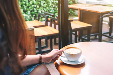 Closeup image of a woman holding a cup of hot coffee on table