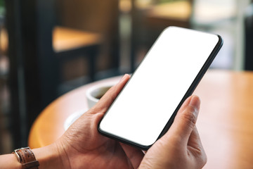 Mockup image of hands holding black mobile phone with blank desktop screen with coffee cup on the table