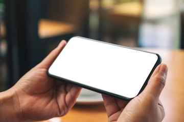 Mockup image of hands holding black mobile phone with blank desktop screen with coffee cup on the table