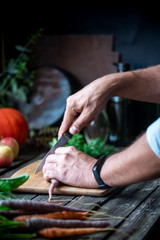 Man cuts freshly picked vegetables in the kitchen, rustic style. Male hands cooking fresh vegetables, vegetarian food, rustic lifestyle.