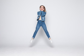 Full length portrait of a cheerful young woman jumping and celebrating over gray background