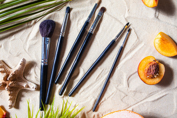 Charming beach. Black stylish makeup brushes with bright fruits, starfish, and palm leaves lie on...