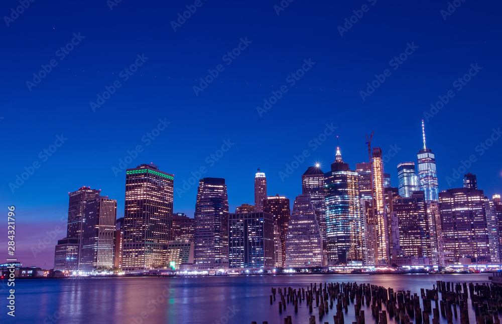Aufkleber View from the water of the bay on the night city center of New York at sunset. Skyscrapers glowing in the dark against the sunset sky.