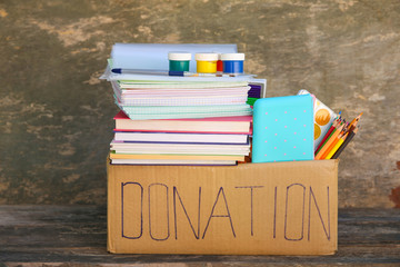 Donation box with school supplies on old wooden background.