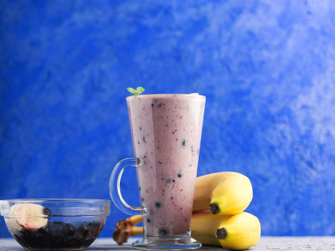 Glass mug of blueberry and banana smoothie on blue background
