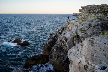 Lone fisherman throwing his angle off a high cliff of the rocky coastline into the wavy Black Sea.
