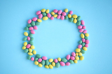 Colored sweets, peanut covered with glaze on blue background composition, round shape, frame.