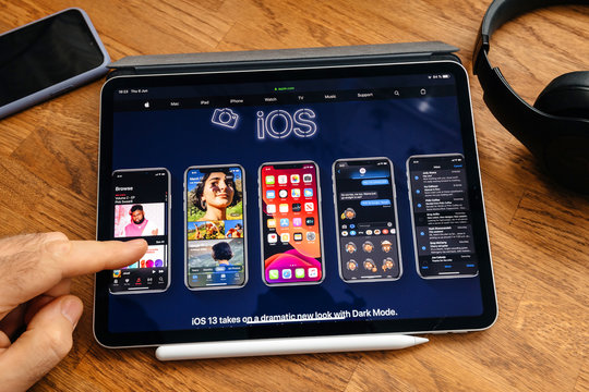 Paris, France - Jun 6, 2019: Man reading on Apple iPad Pro tablet about latest announcement of at Apple Worldwide Developers Conference WWDC - showing the iOS update on multiple iPhone XS