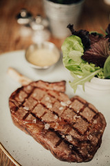 A close up shot of a beef fillet steak with sea salt served on a ceramic plate with salad and sauce. Concept of restaurant, food and culinary.